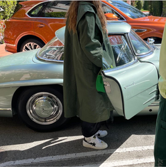 model figure wearing a long green trench coat and bapesta trainers, next to a vintage mercedes truck in a car parking lot