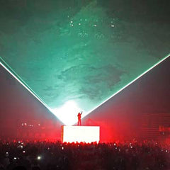 man stands on stage or podium with a sea of people making up the crowd, a laser separates the lighting behind the stage green and red