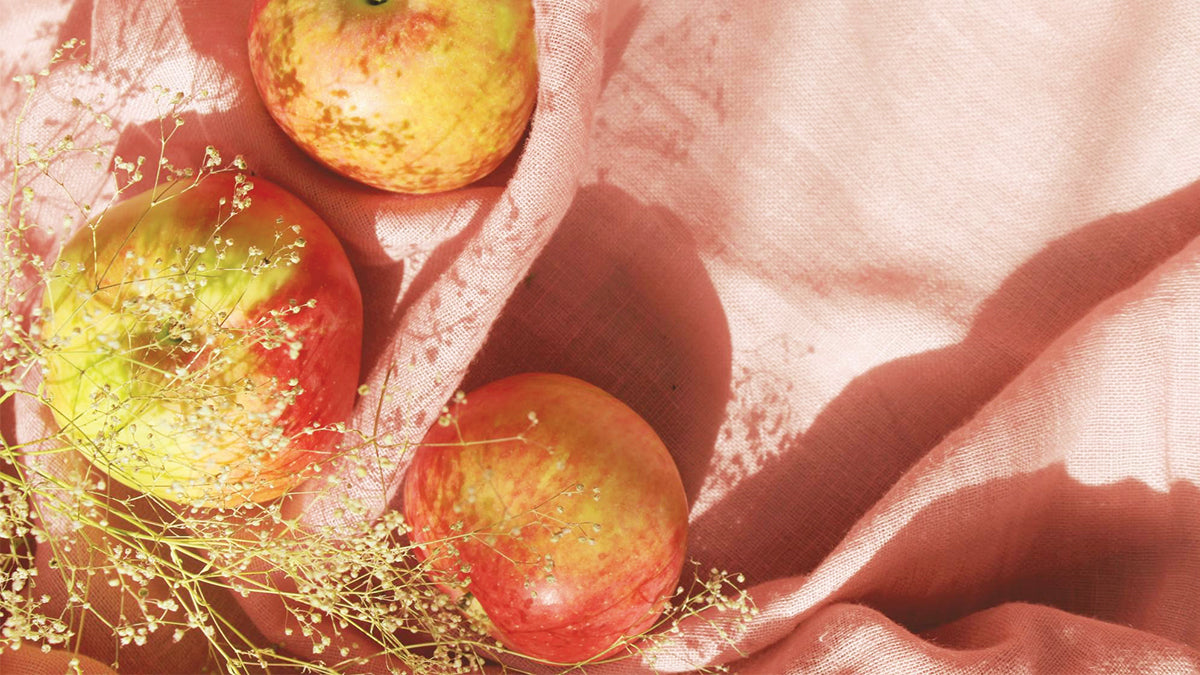 Three apples lay on a light pink linen cloth. 