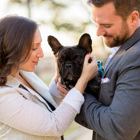 A man and a woman embrace a french bulldog while smiling at the dog