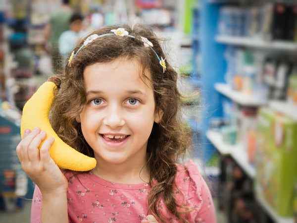 A child holding a banana plush as if it were a telephone