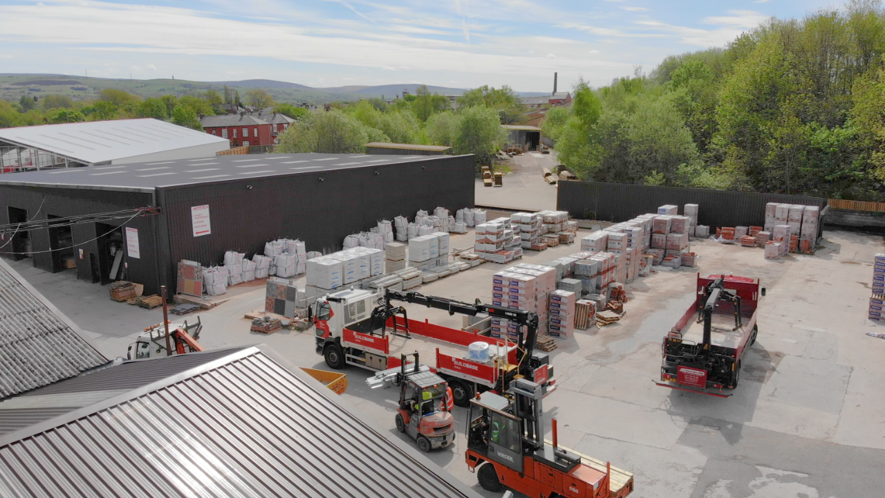 A bustling storage yard with indoor and outdoor facilities, many pieces of equipment such as forklift, hydraulic loader crane trucks, and a heavy side loader forklift.