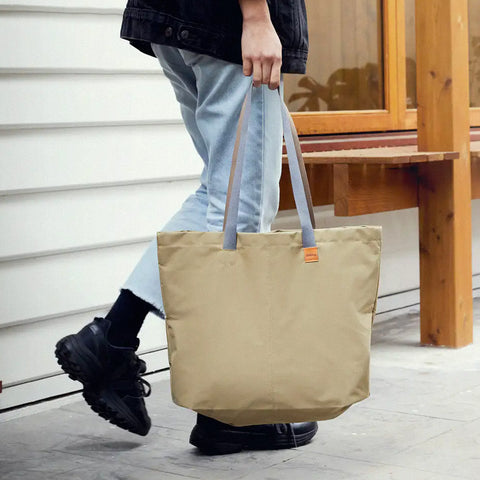 A person holding a Market Tote in Khaki by the handles as they walk