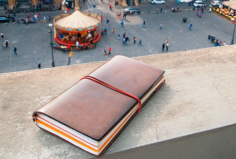 A Traveler's Notebook, full of memories, sits on a ledge overlooking a busy town square