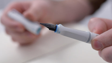 A close-up of a white fountain pen with blue ink dried around the nib and grip section