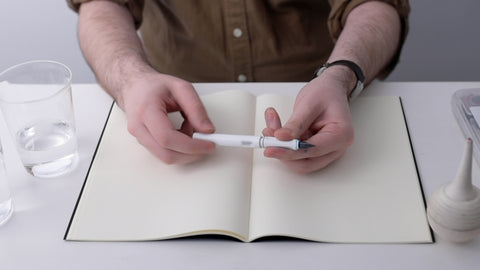 A pair of hands twisting the body of a fountain pen to remove it from the grip section