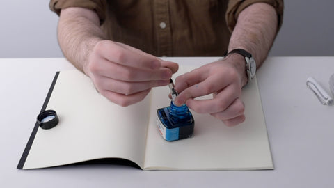 Filling a fountain pen with bottled ink (fountain pen held delicately in fingertips over the bottle)