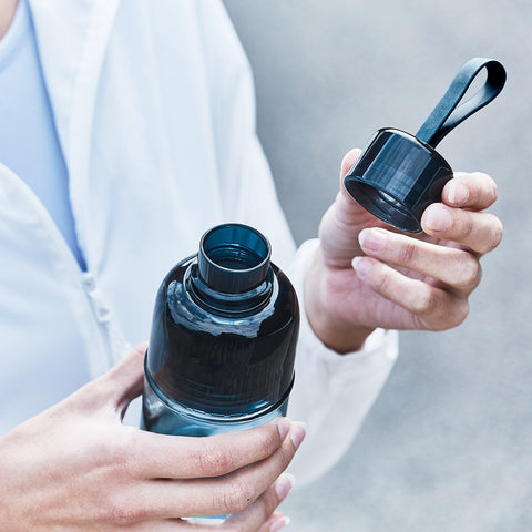 Kinto Workout Bottle in Blue, held in a person's hands with the lid removed 