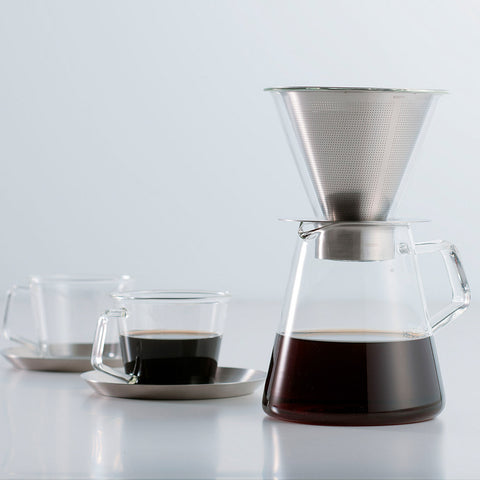 Kinto's Carat Pourover Coffee Maker sat on a bench with a full pot of dark coffee, next to a Kinto Cast glass of matching coffee