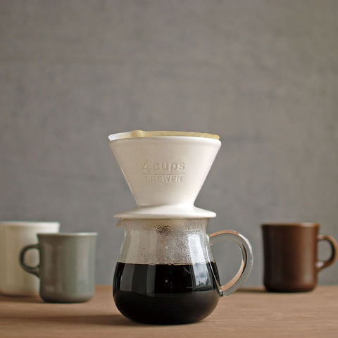 Kinto's SCS Porcelain Pourover Coffee Brewer sat on top of an SCS Serving Jug that's got a belly full of deep, dark coffee