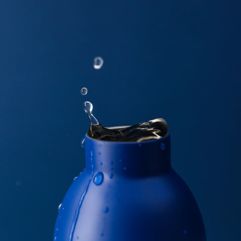 A close-up of a 24Bottles Clima drink bottle in Pacific Beach finish, with water caught mid-splash up and out of the mouth