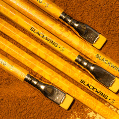 Blackwing Vol 3 pencils, with turmeric yellow finish, laid on brown dust that looks like cumin