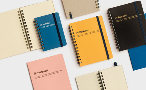 [img: a flat lay of Rollbahn notebooks with yellow, pink, blue and black covers]