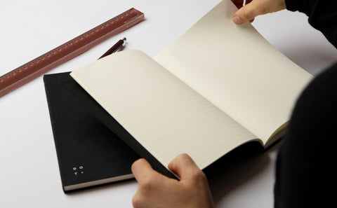 A person holding a Studio Milligram notebook open to show its ruled pages