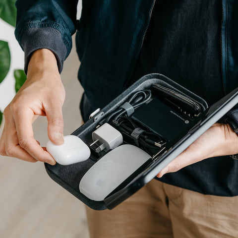 Orbitkey Nest Desk Organiser | Milligram [img: an Orbitkey Nest with its top open, held in one hand as another puts an AirPor case inside alongside an Apple mouse, USB charger and sundry cables]