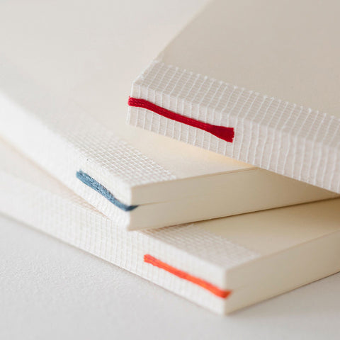 A close-up of three Midori notebooks stacked loosely on top of each other, each with an exposed cheesecloth tape on the spine