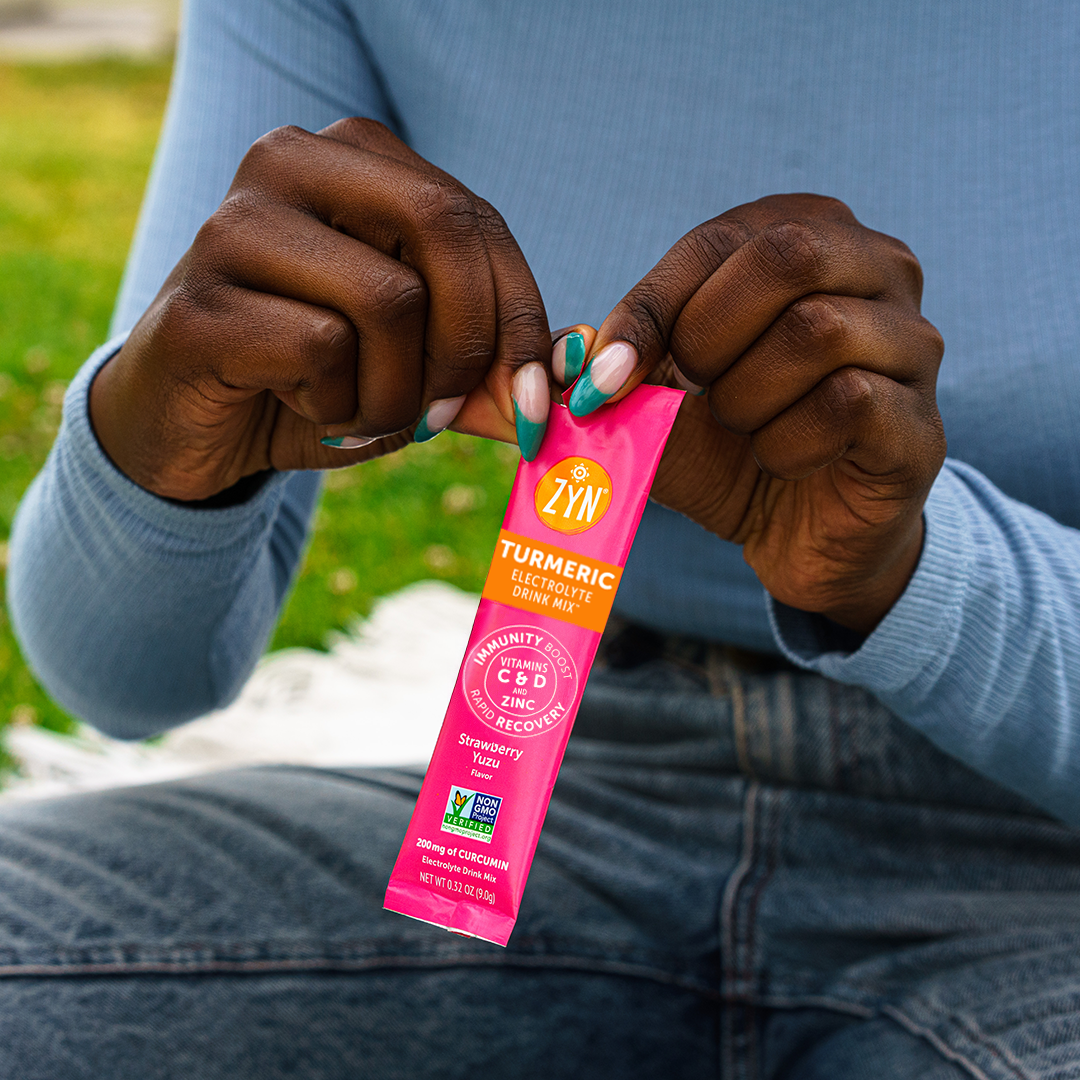 Person holding a Zyn Turmeric Electrolyte Drink Mix sachet, Strawberry Yuzu flavor.
