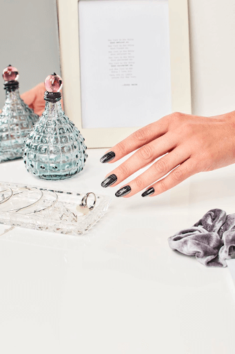 Hand with black and grey nail polish reaches for a ring in a dish