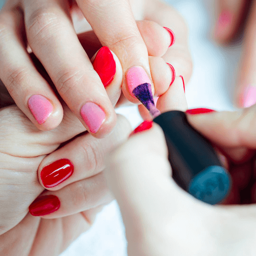 Person with red nails paints another person’s nails pink