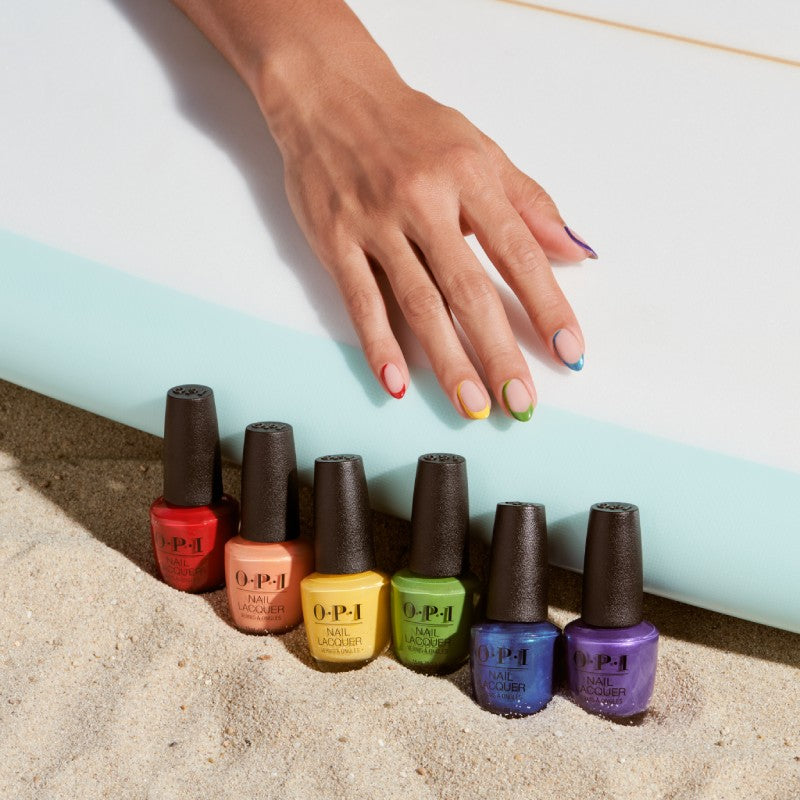 a hand reaches for a row of OPI nail lacquer lined up next to a surfboard on sand