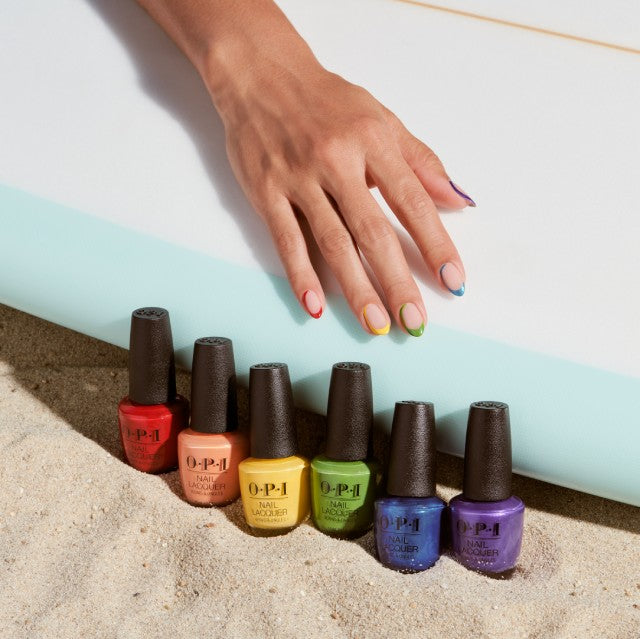 a hand reaching for a row of OPI nail lacquer next to a surfboard on sand