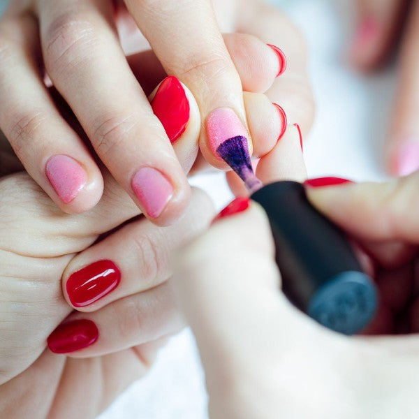 Person applying pink nail polish to someone’s nails