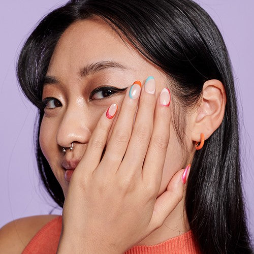 a woman shows her colorful nail art with a hand to her face