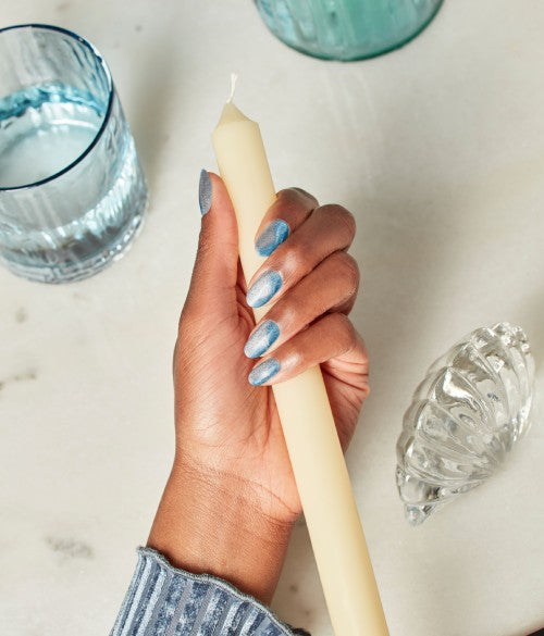 Hand holding candle stick with shimmery blue nails