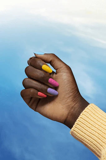 Black woman’s hand with different colored nails in front of blue sky