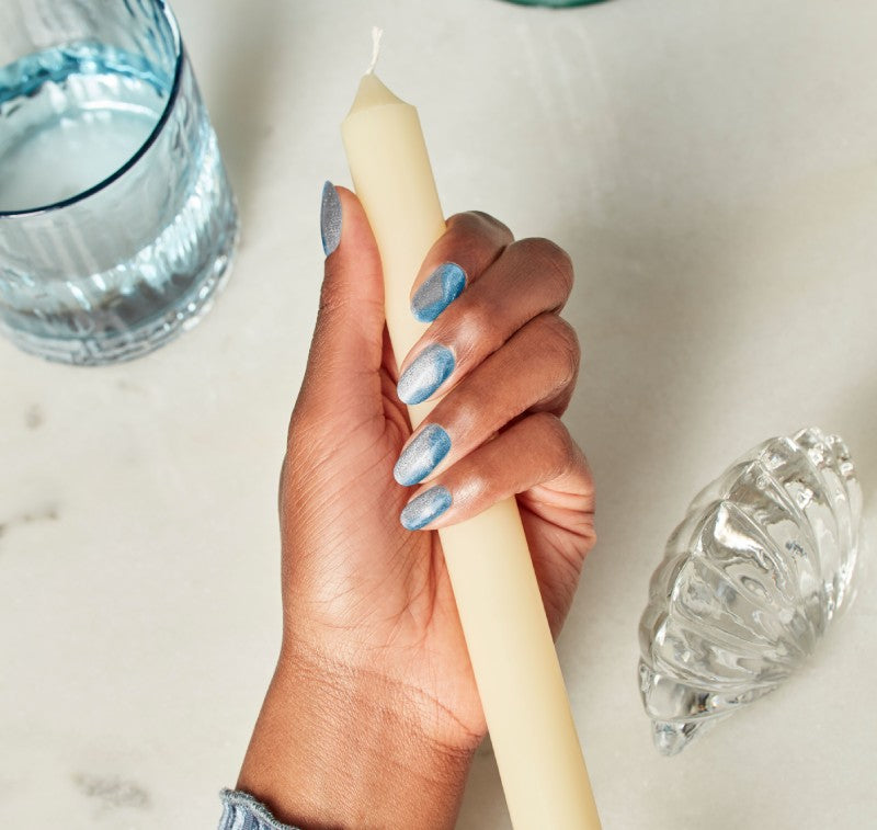 Hand with blue nail art holding candle