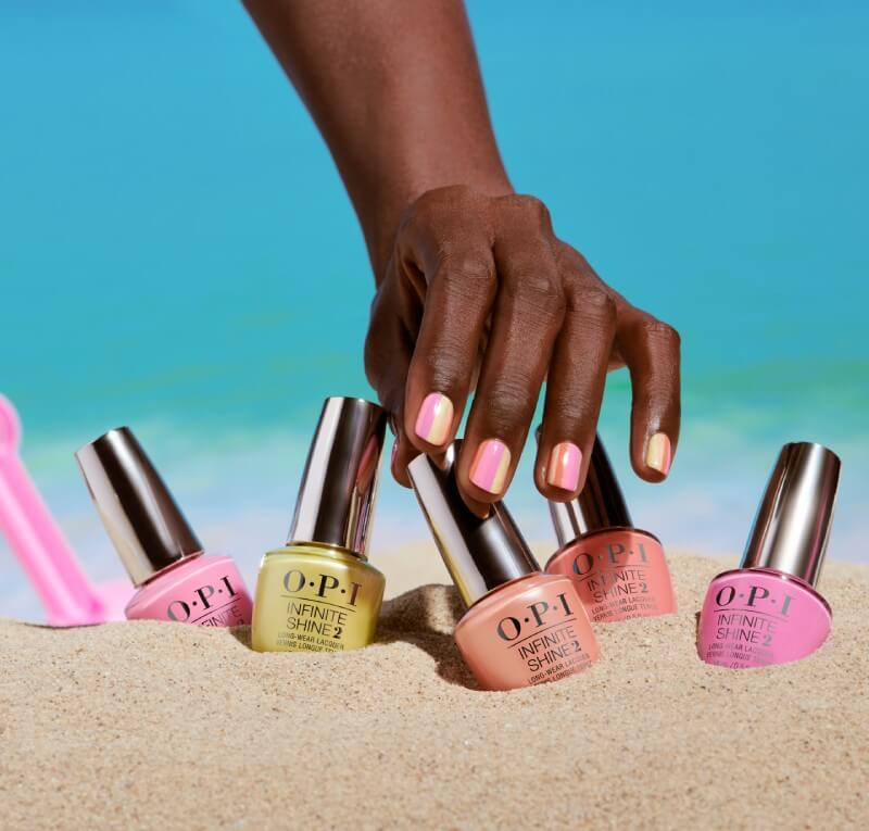 Hand with bright nail polish reaches for nail polish bottles in the sand
