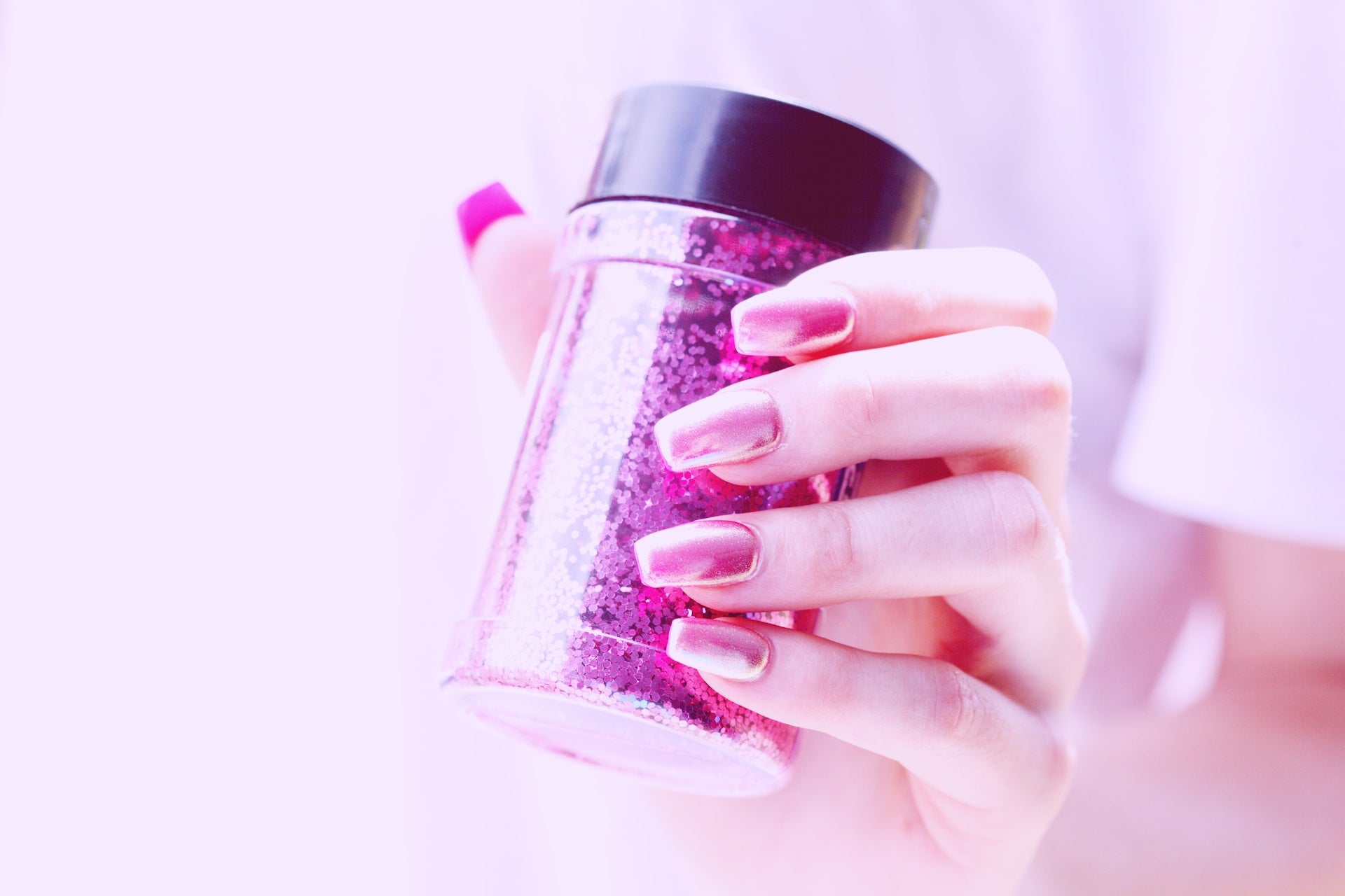Hand with metallic magenta nails holding glitter