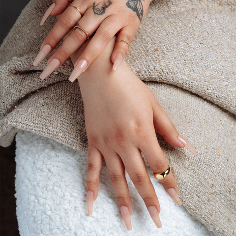 Hand with nude colored nail extensions and ring against beige cloth