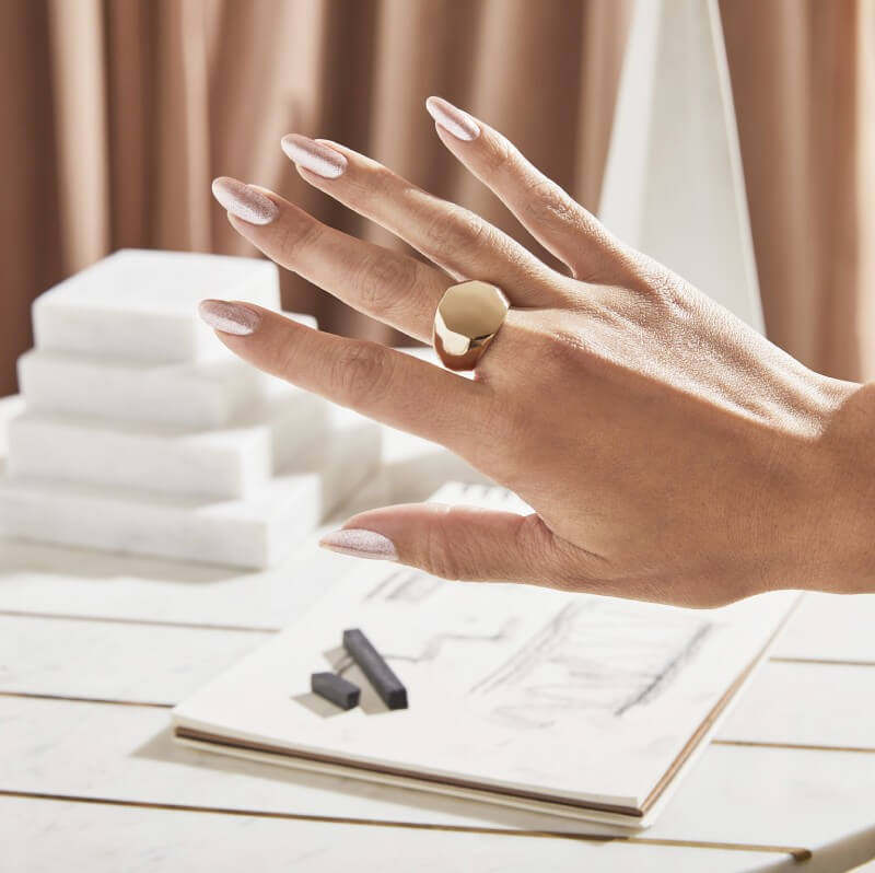 Hand with gold statement ring shows off metallic gold nails