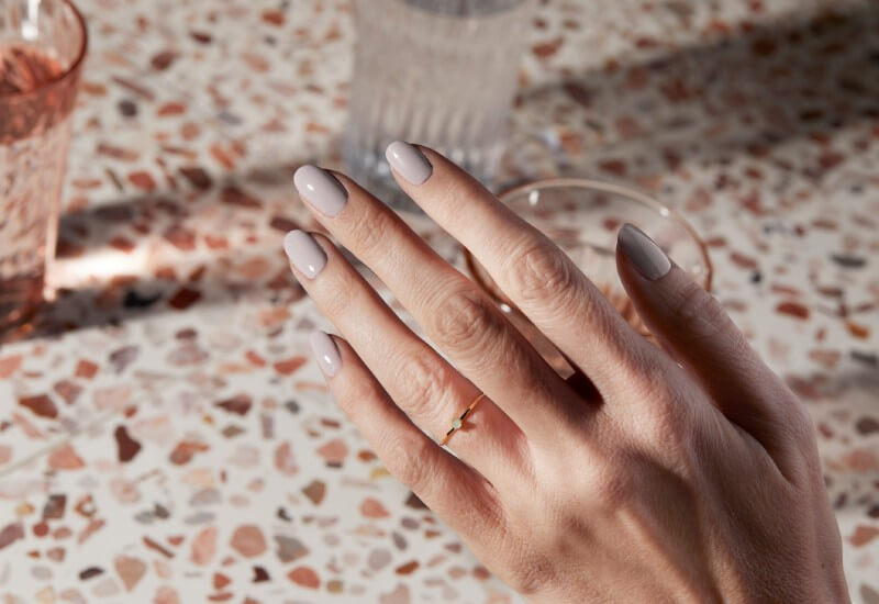 Hand with dainty ring shows taupe nails