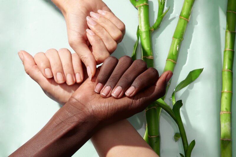 Three hands show healthy nails next to bamboo