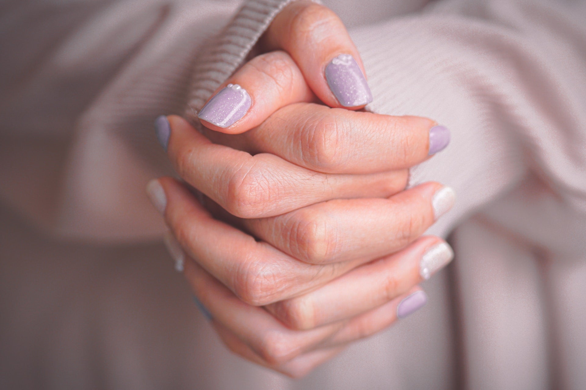 Hands folded showing lavender nails with pearls