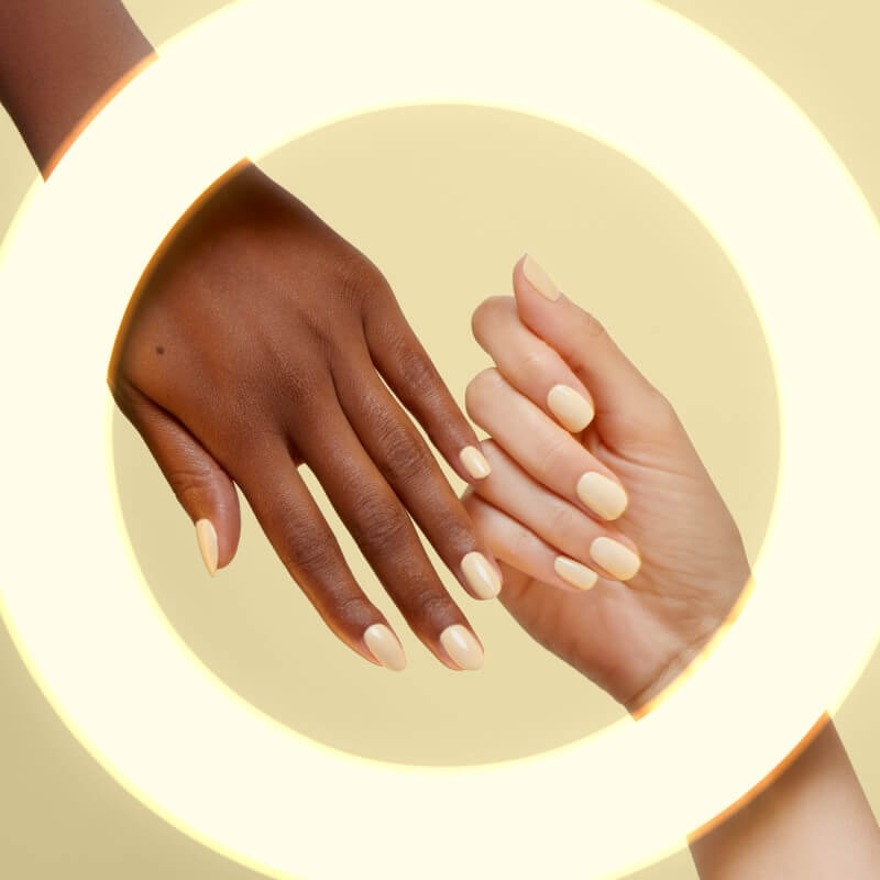 Two hands of different complexions show light yellow nails behind yellow ring light
