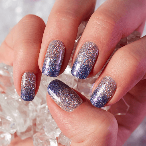 Hand with glitter ombre pink to purple nails holding crystals