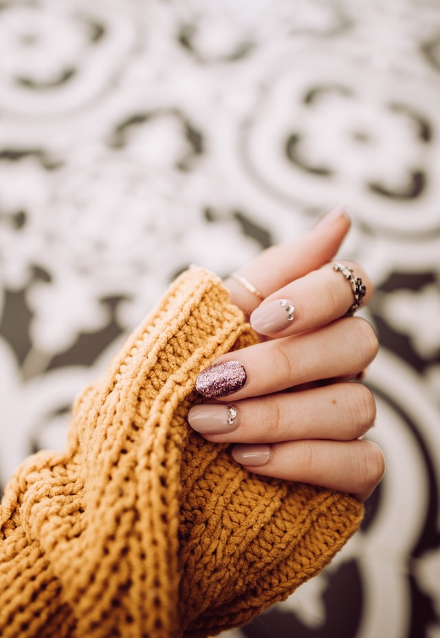 Hand in a yellow sweater with pink and nude nails with rhinestones