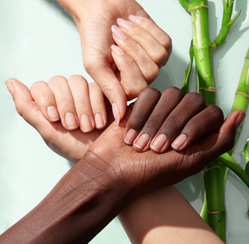 Three hands of different complexions show strong, natural nails with bamboo behind them