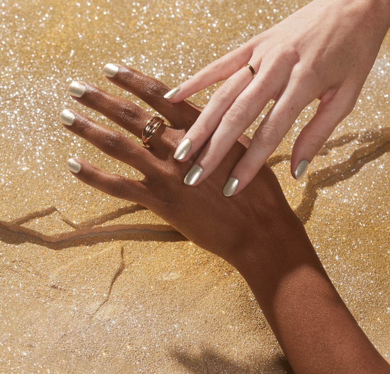 Two different people show gold nails over a bed of gold powder