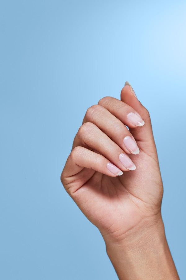 Hand with healthy nails in a loose fist with a blue background