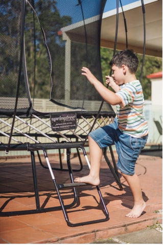 A child stepping on a trampoline ladder.