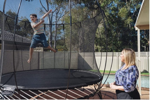 A mother watching her son jump in mid-air on a Springfree Trampoline.