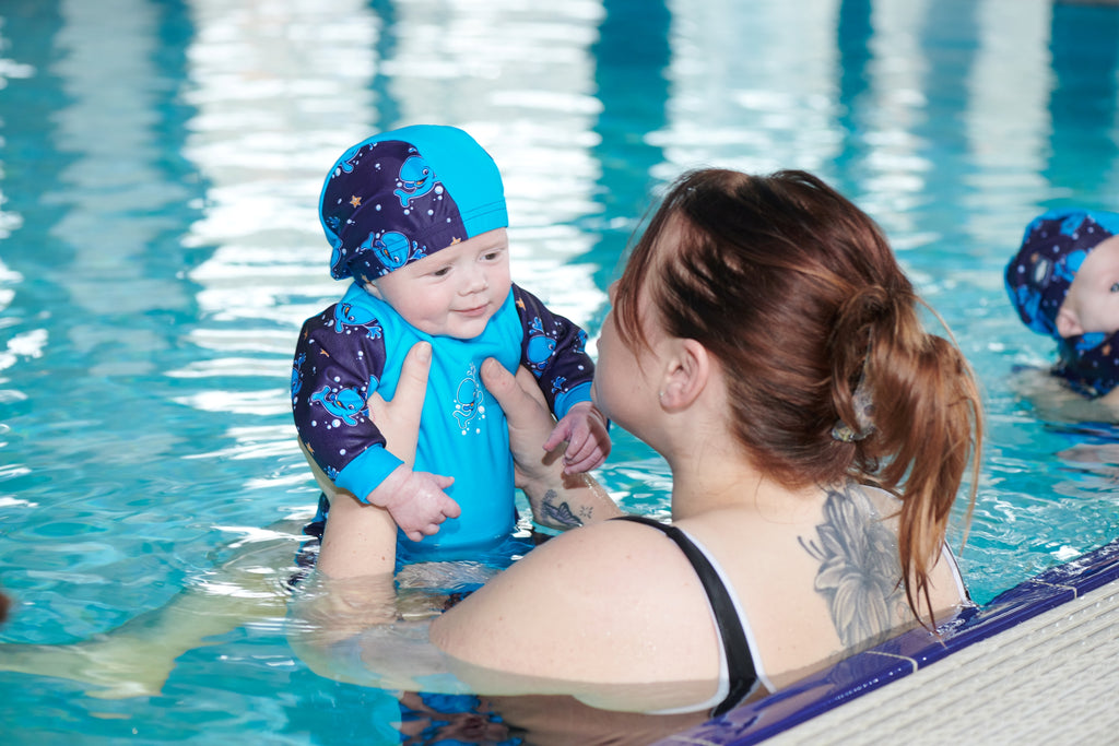 Baby wearing a Warm in One wet suit and a swim hat with their carer in the swimming pool.