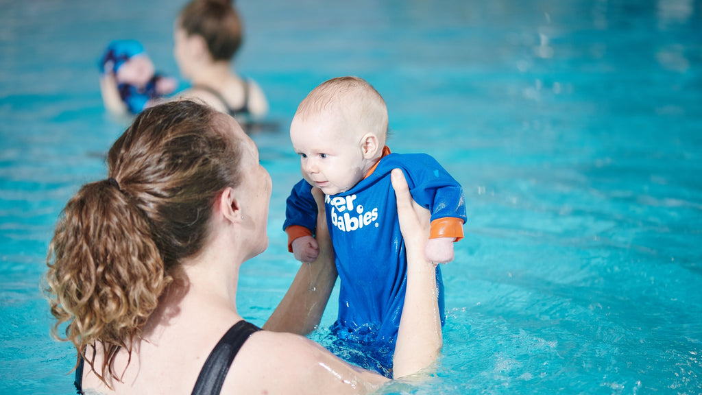 Image of baby wearing a Warm in One wetsuit, with their carer during a Water Babies lesson.