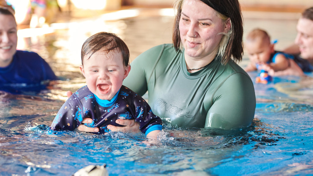Little one swimming in a Happy Nappy wetsuit during a Water Babies lesson.