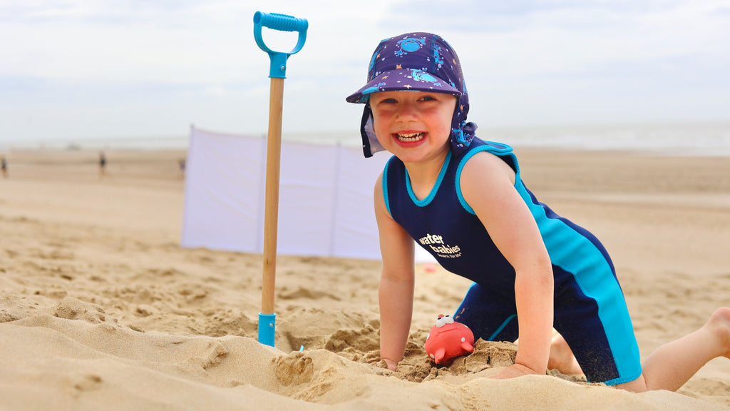 Toddler in the beach, wearing a toddlers wet suit and a legionnaire sun hat.