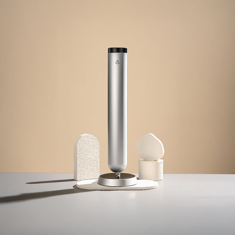 A slim, tall diffuser with a matte black finish, resting on a neutral background with simple geometric stone stands.